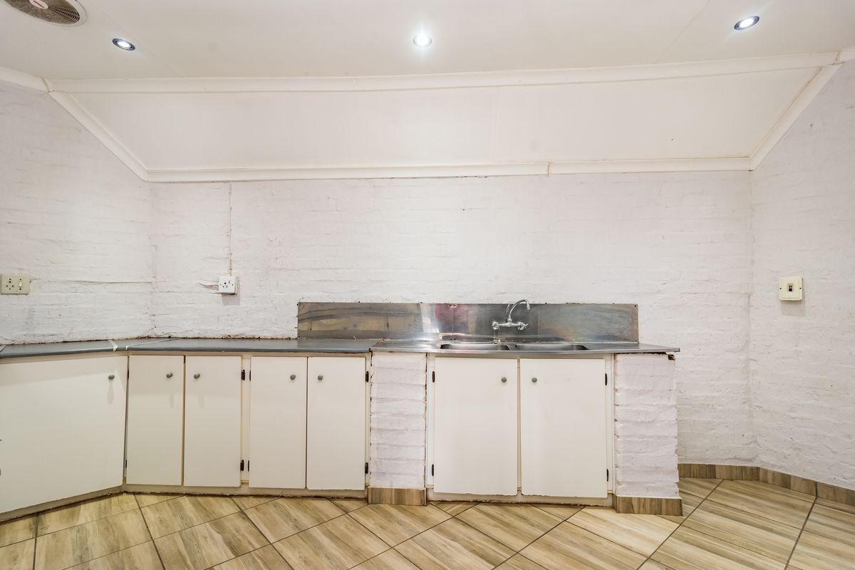 A functional kitchen area featuring white built-in cabinetry, a stainless steel sink, and tiled flooring, ready for a modern renovation.