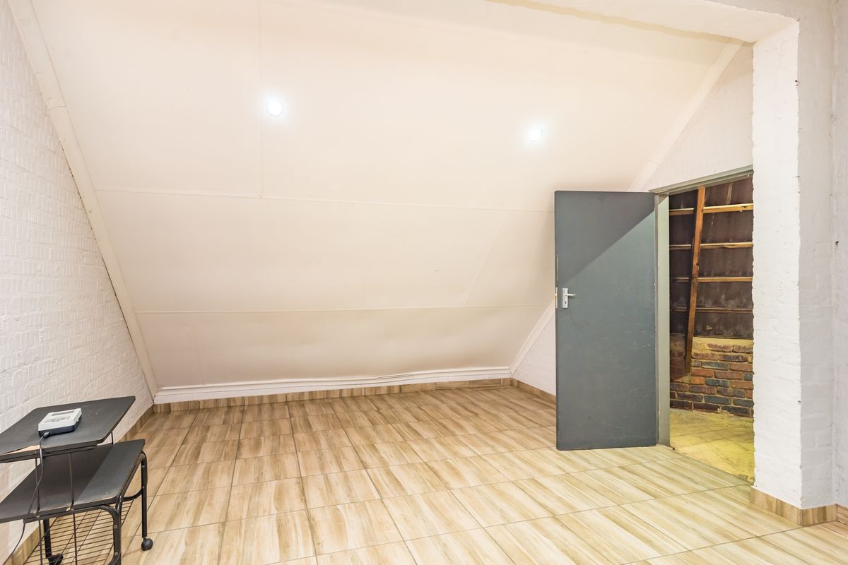 An empty attic-style bedroom featuring sloped ceilings, tiled flooring, and a painted brick wall, offering a blank canvas for renovation.