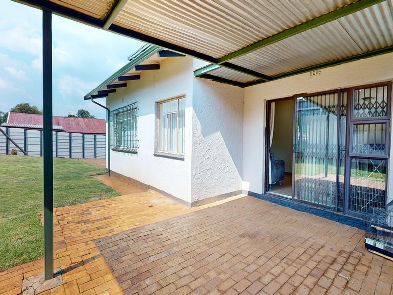 Covered patio area featuring brick paving and direct access to the interior through a sliding glass door with security gate.