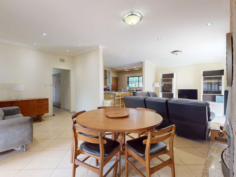Spacious open-plan living and dining area featuring tiled floors, recessed lighting, and a stone feature wall, seamlessly flowing into the kitchen.