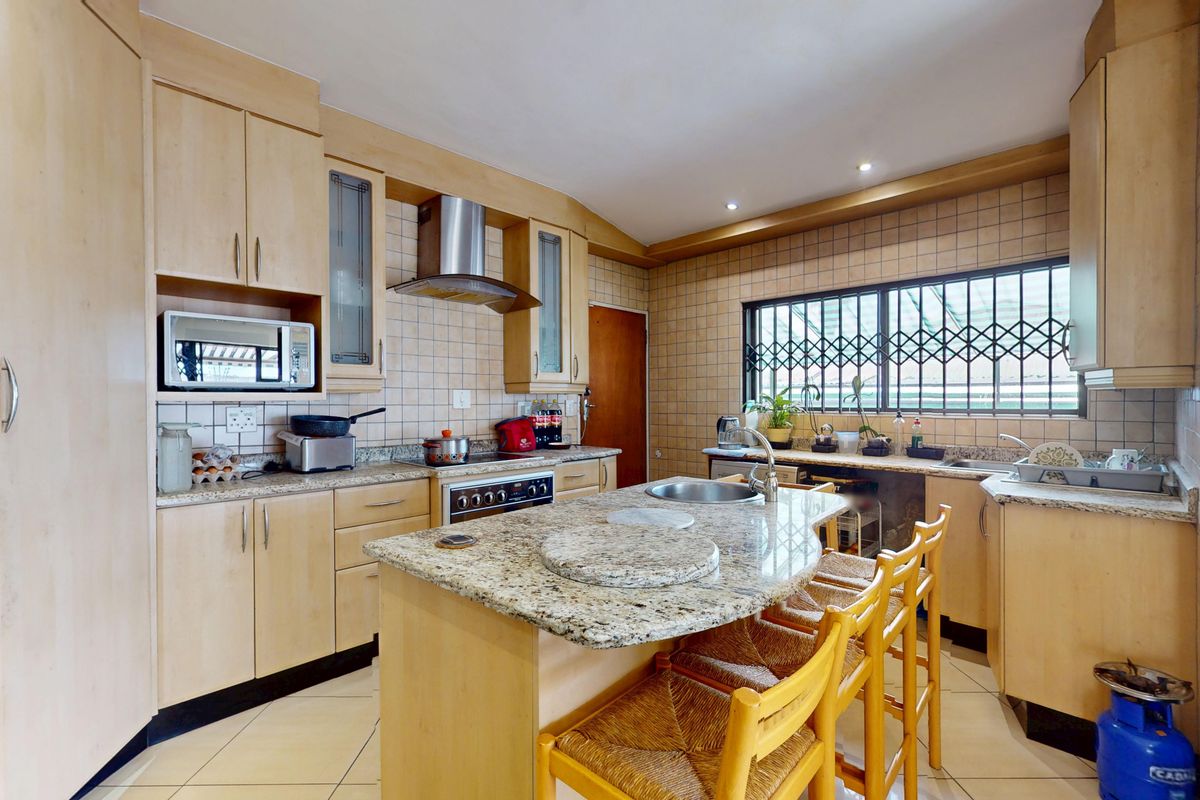 A functional kitchen featuring light wood cabinetry, granite countertops, a central island with a sink, and a tiled backsplash with integrated appliances.