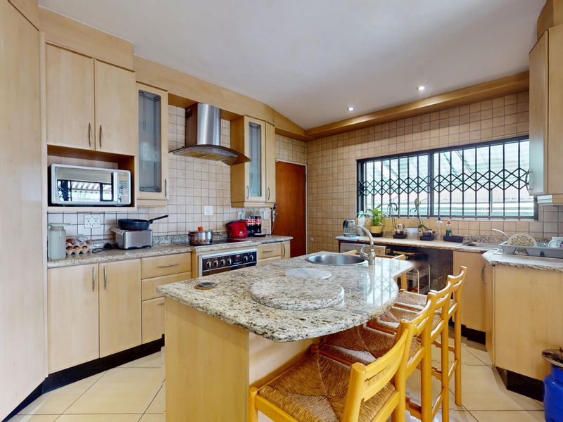 A functional kitchen featuring light wood cabinetry, granite countertops, a central island with a sink, and a tiled backsplash with integrated appliances.