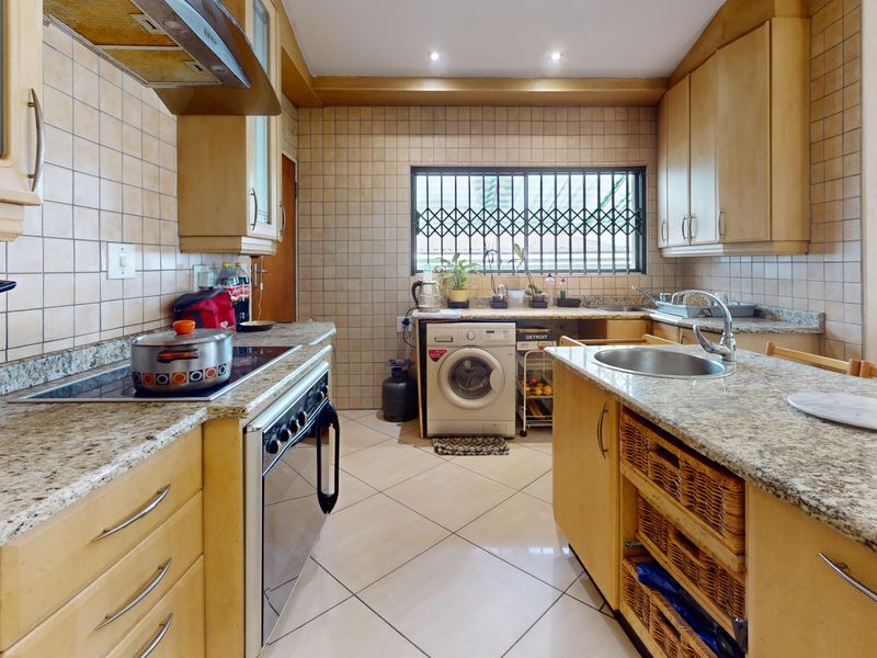Functional kitchen featuring granite countertops, built-in cabinetry, electric hob, oven, and a tiled splashback with a security-fitted window.