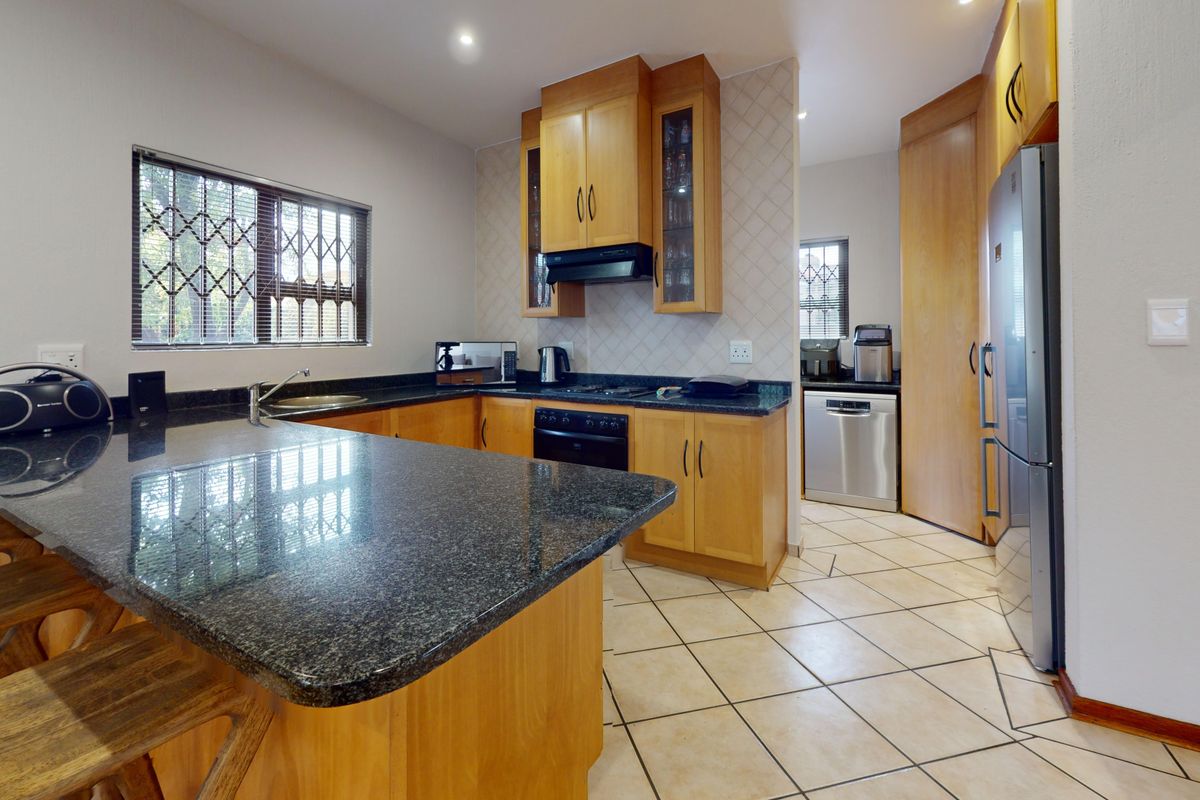 A functional kitchen featuring wooden cabinetry, granite countertops, tiled flooring, and a breakfast nook, with a separate scullery area visible in the background.