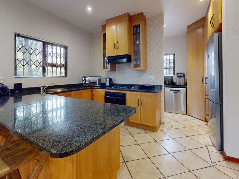 A functional kitchen featuring wooden cabinetry, granite countertops, tiled flooring, and a breakfast nook, with a separate scullery area visible in the background.