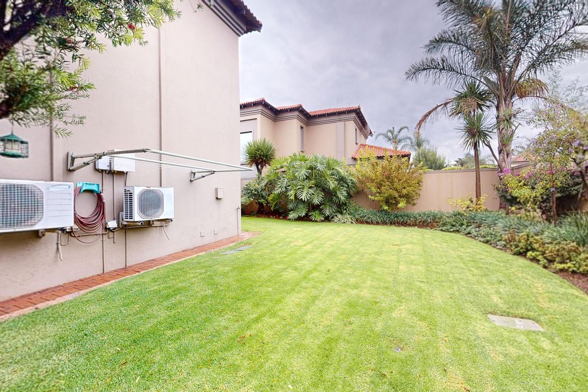 A well-maintained rear garden featuring a manicured lawn, established landscaping, and exterior wall-mounted utility fixtures including air conditioning units.