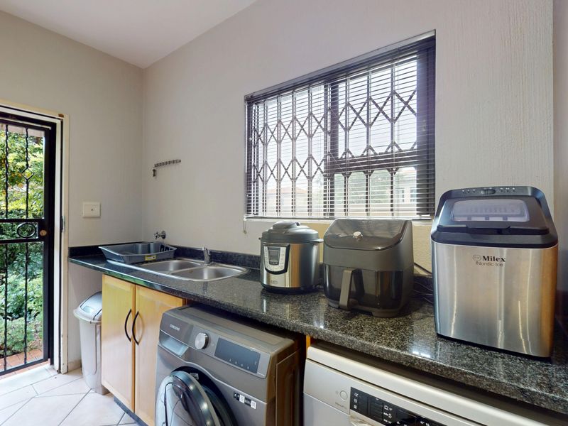 Functional laundry area featuring granite countertops, a double sink, tiled flooring, and direct access to the garden through a secure exterior door.