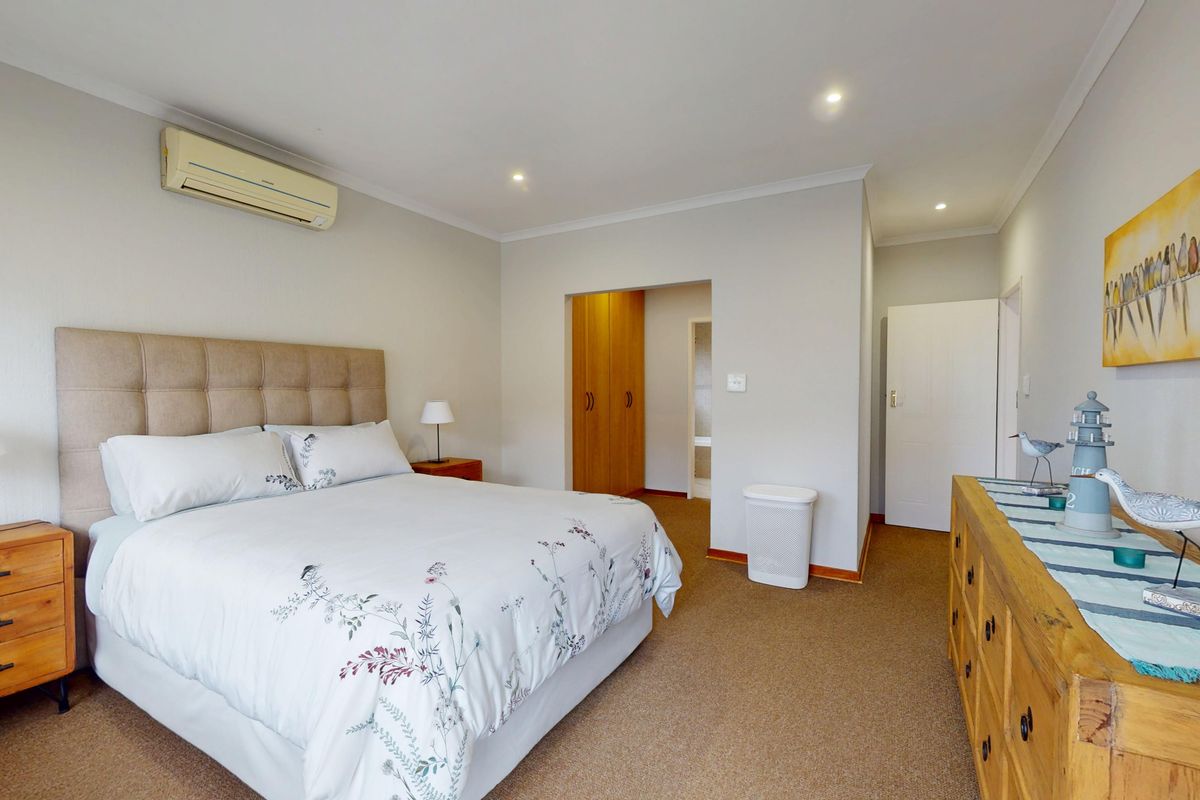 A well-maintained bedroom featuring neutral walls, carpeted flooring, built-in cupboards, and a wall-mounted air conditioning unit.