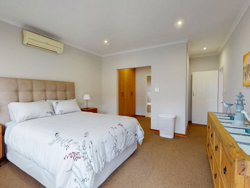 A well-maintained bedroom featuring neutral walls, carpeted flooring, built-in cupboards, and a wall-mounted air conditioning unit.