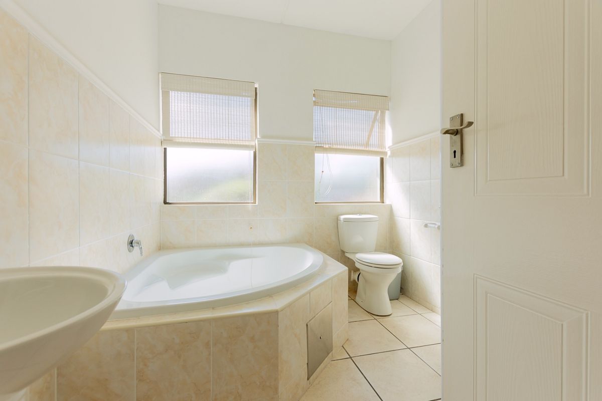 A functional bathroom featuring a corner bathtub, pedestal basin, and toilet with neutral wall and floor tiling.
