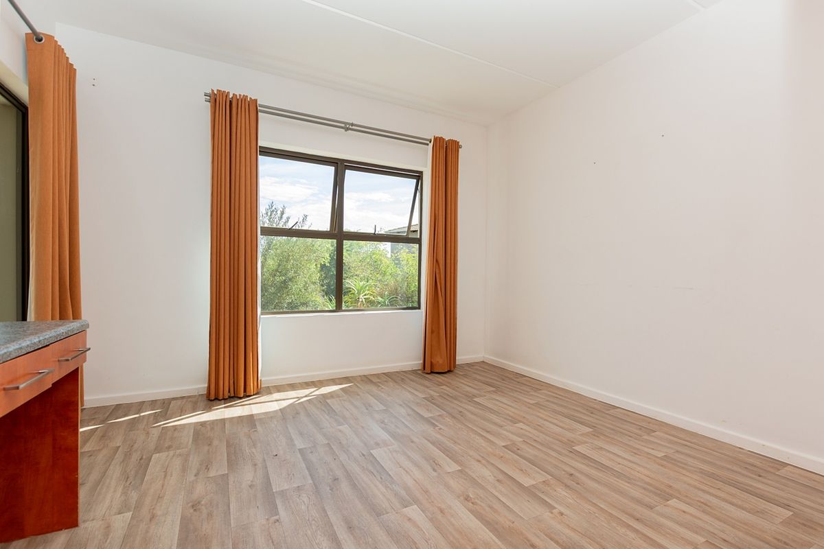 A bright, empty bedroom featuring modern laminate flooring, a large aluminium window, and a built-in vanity unit.