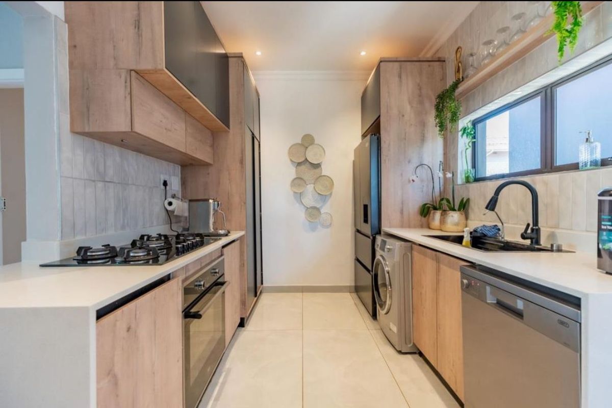Modern galley-style kitchen featuring wood-grain cabinetry, stone countertops, gas hob, built-in oven, and integrated appliances with a clean, contemporary finish.
