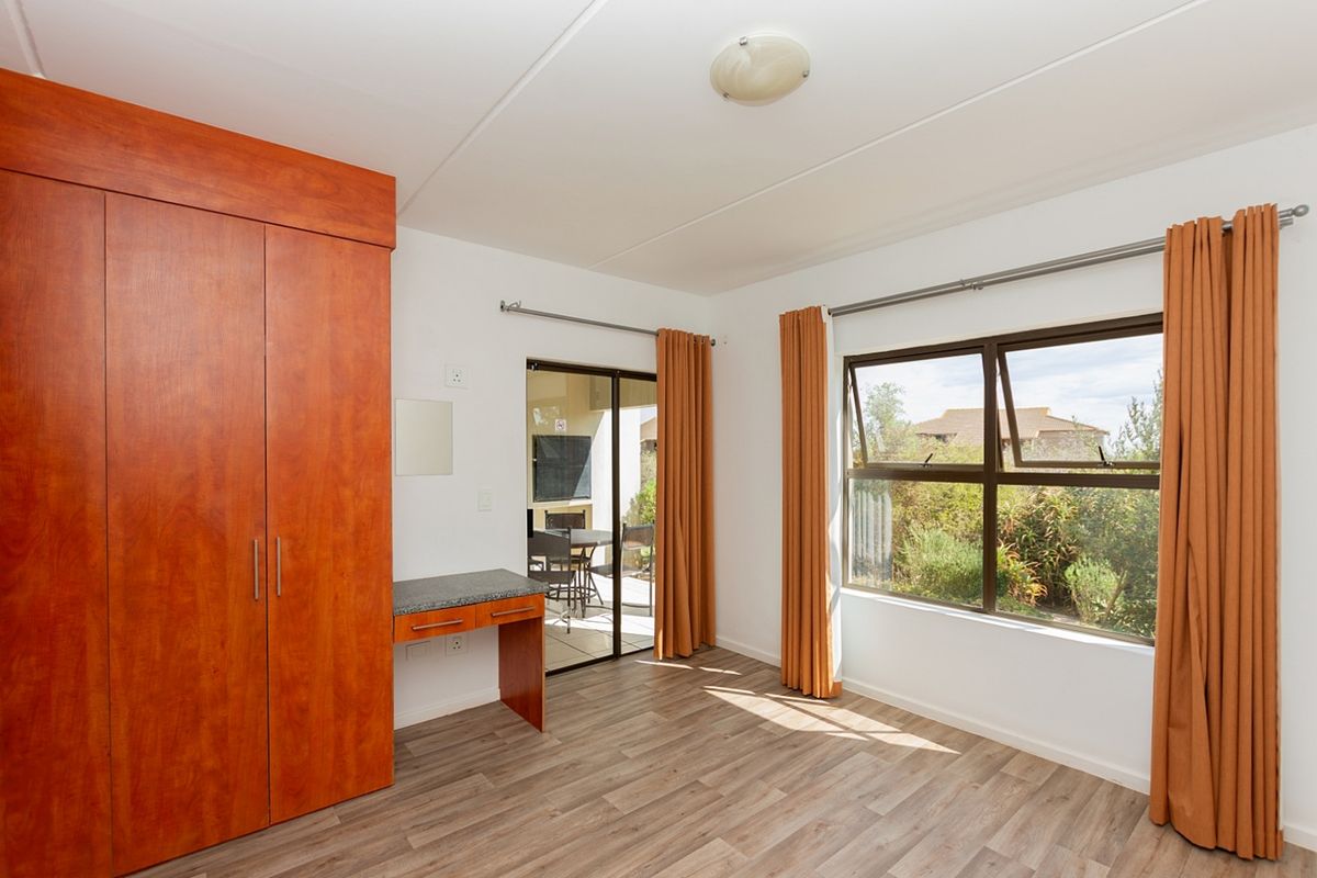 A bright bedroom featuring built-in wooden cabinetry, a vanity area, laminate flooring, and direct access to an outdoor patio through a sliding glass door.