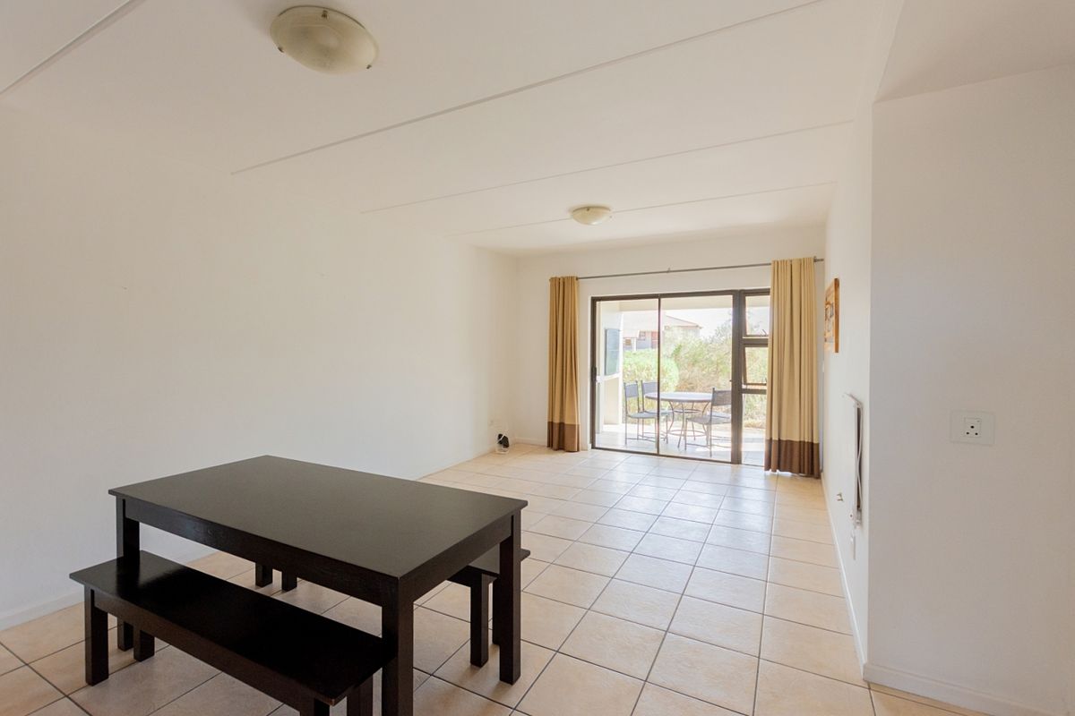 A bright, open-plan living area featuring neutral tiled flooring and a sliding glass door that provides direct access to an outdoor patio space.