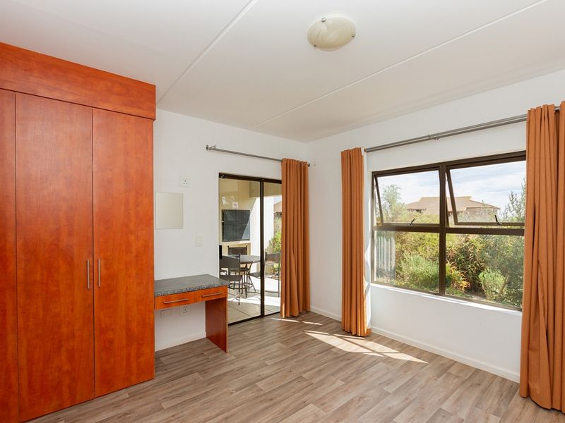 A bright bedroom featuring built-in wooden cabinetry, a vanity area, laminate flooring, and direct access to an outdoor patio through a sliding glass door.