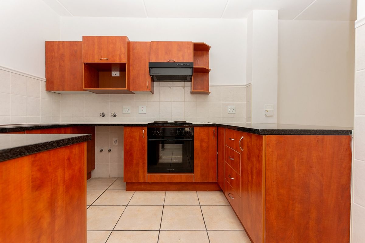 A functional kitchen featuring wood-finish cabinetry, granite countertops, built-in oven, hob, and extractor fan with neutral tiled flooring and splashbacks.