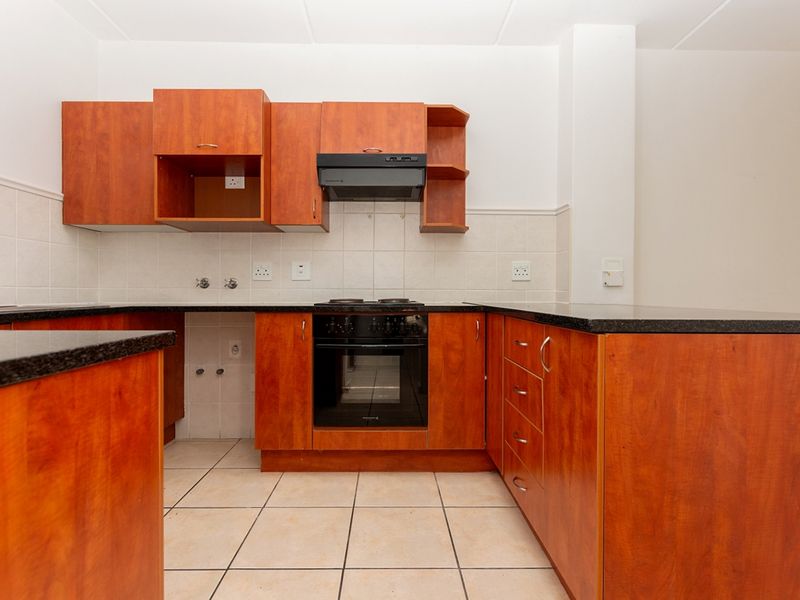 A functional kitchen featuring wood-finish cabinetry, granite countertops, built-in oven, hob, and extractor fan with neutral tiled flooring and splashbacks.