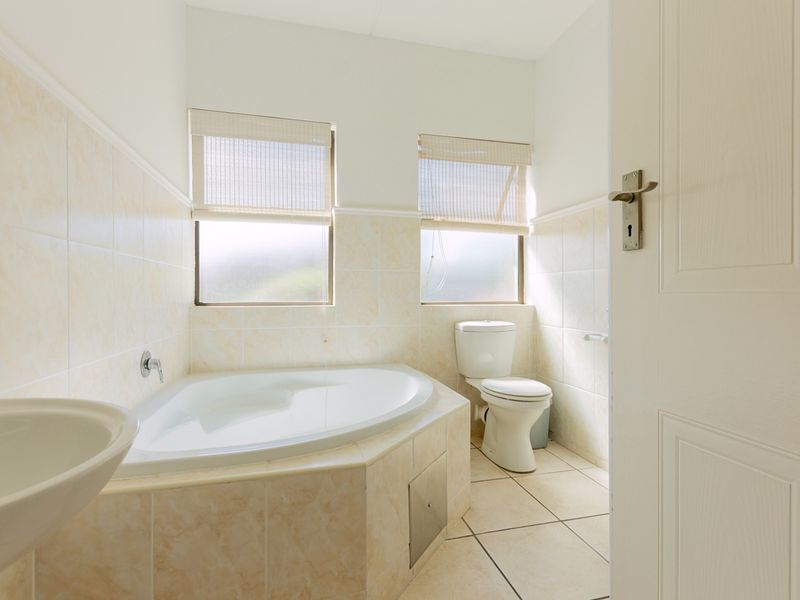 A functional bathroom featuring a corner bathtub, pedestal basin, and toilet with neutral wall and floor tiling.