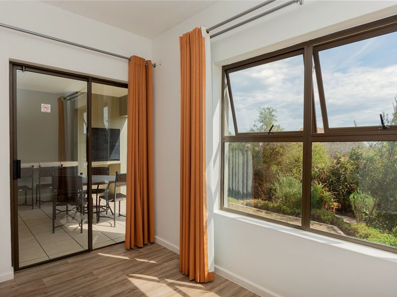 Bright living area featuring laminate flooring, a large top-hung window, and a sliding glass door providing access to an outdoor patio space.