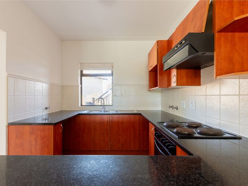 A functional kitchen featuring dark granite countertops, wood-finish cabinetry, a built-in electric hob, oven, and extractor fan with a tiled splashback.