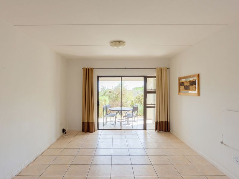 An empty, neutrally painted living room featuring tiled flooring and a sliding glass door that opens onto a patio area.