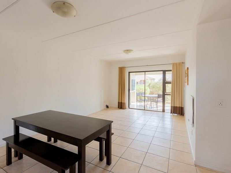 A bright, open-plan living area featuring neutral tiled flooring and a sliding glass door that provides direct access to an outdoor patio space.