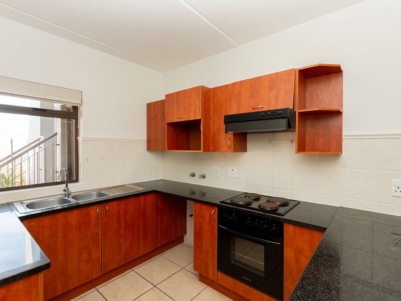 A functional kitchen featuring dark granite countertops, wooden cabinetry, a built-in oven with hob, and a double basin sink with tiled splashback.