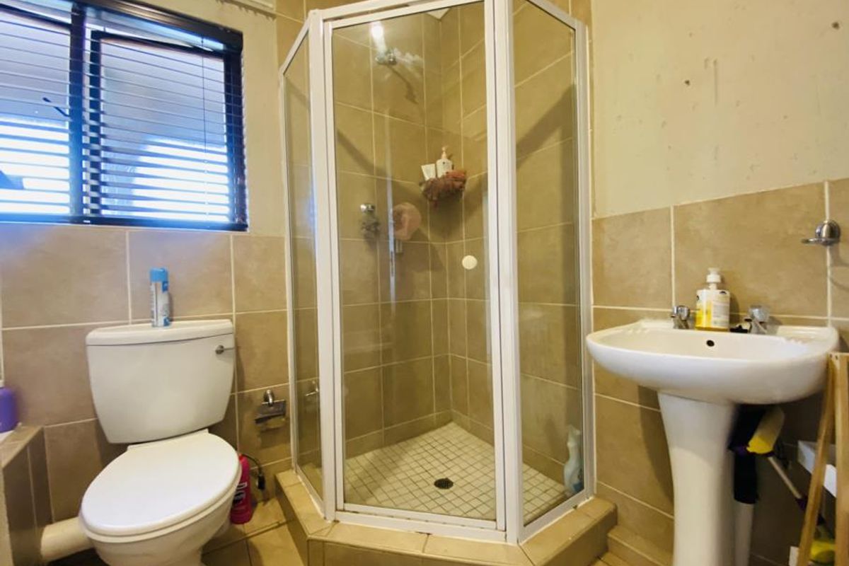 A functional bathroom featuring a corner shower enclosure, pedestal basin, and toilet with neutral wall and floor tiling.
