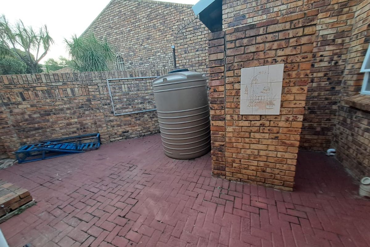 A paved rear courtyard area featuring face brick walls, a water storage tank, and a wall-mounted washing line.