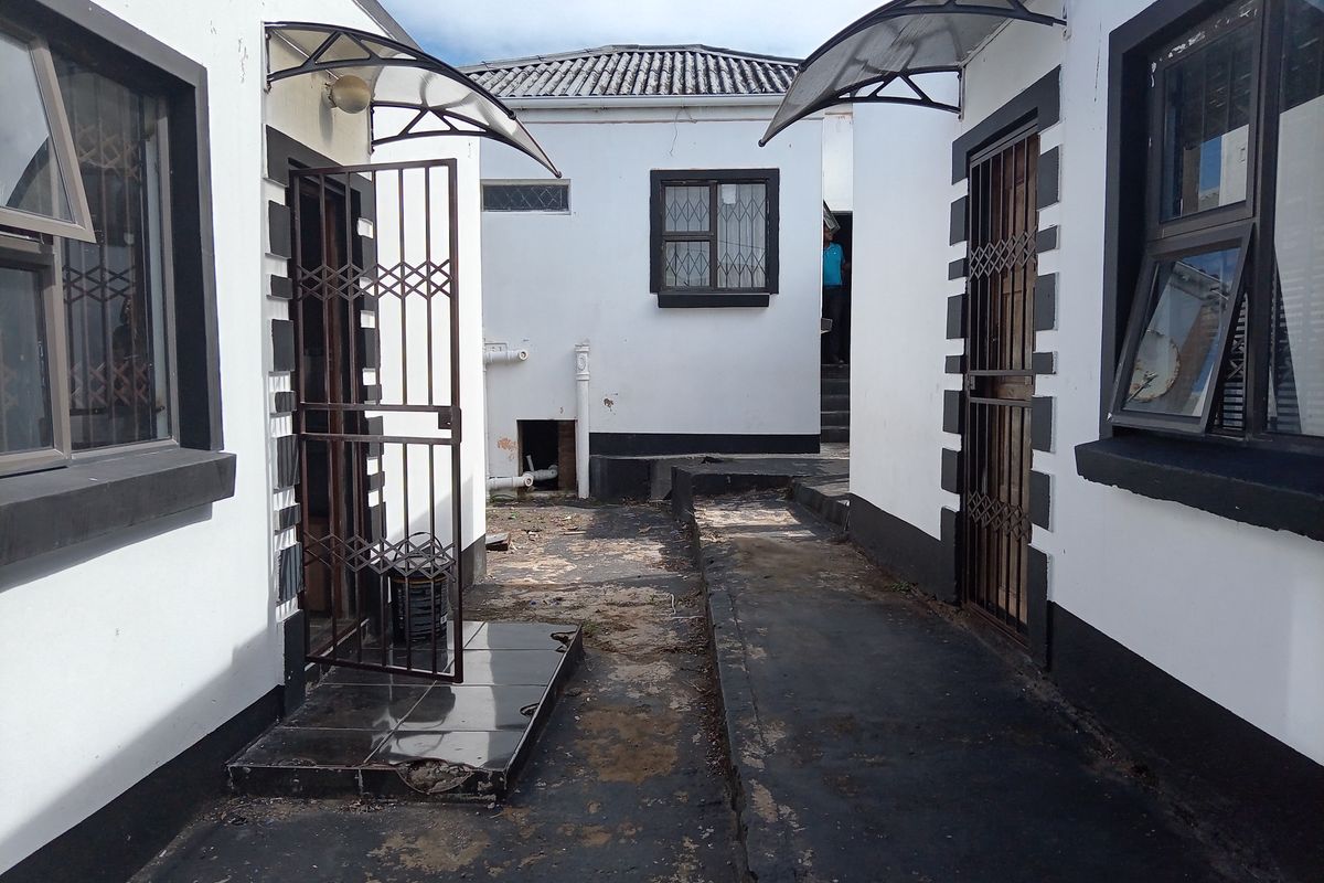 Rear exterior courtyard area featuring concrete paving, security gates, and protective awnings over the doorways.