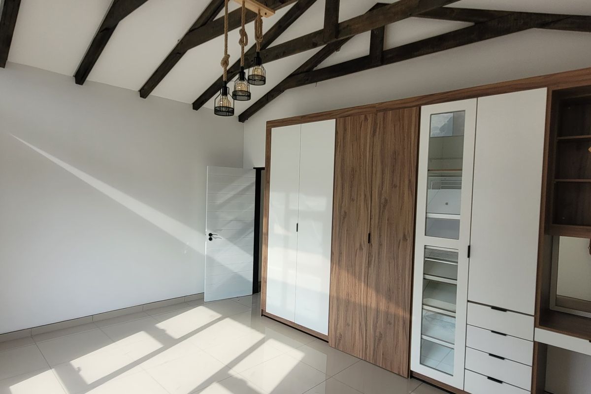 Spacious bedroom featuring high vaulted ceilings with exposed timber beams, modern built-in cabinetry with integrated vanity, and sleek tiled flooring.