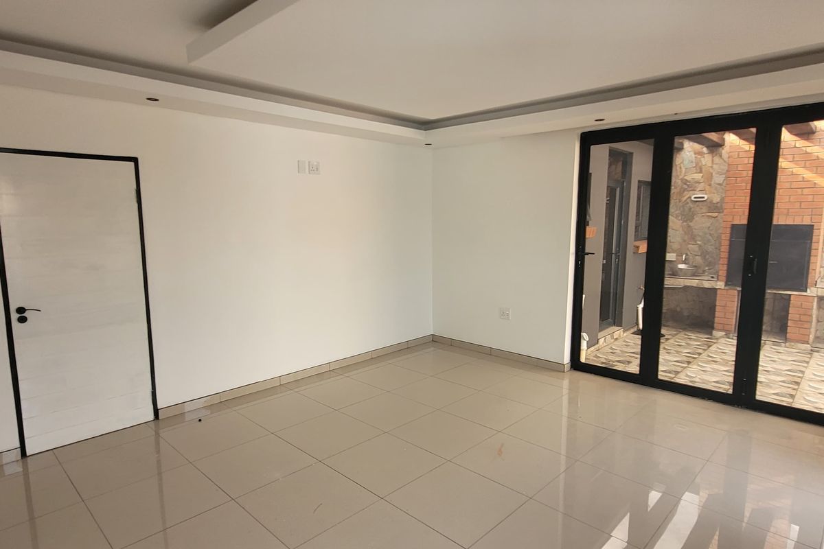 A bright, modern living area featuring neutral tiled floors, recessed ceiling lighting, and large black aluminium sliding doors opening to an outdoor patio.