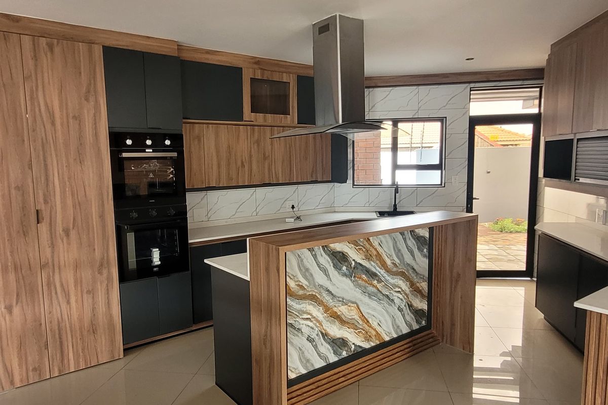Modern kitchen featuring wood-grain and matte black cabinetry, stone countertops, a central island, built-in oven, and a sleek extractor fan.