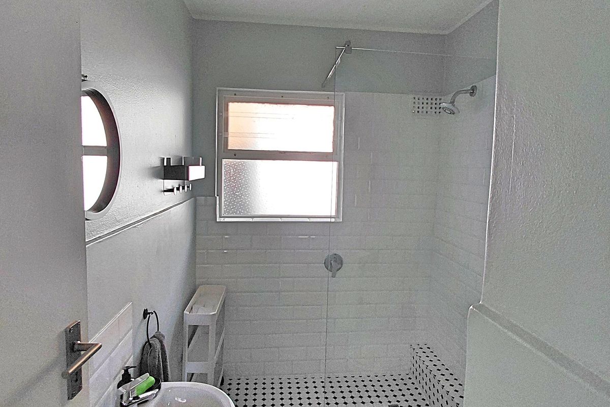 A clean, modern bathroom featuring a walk-in shower with glass screen, subway wall tiling, mosaic floor tiles, and a classic pedestal basin.