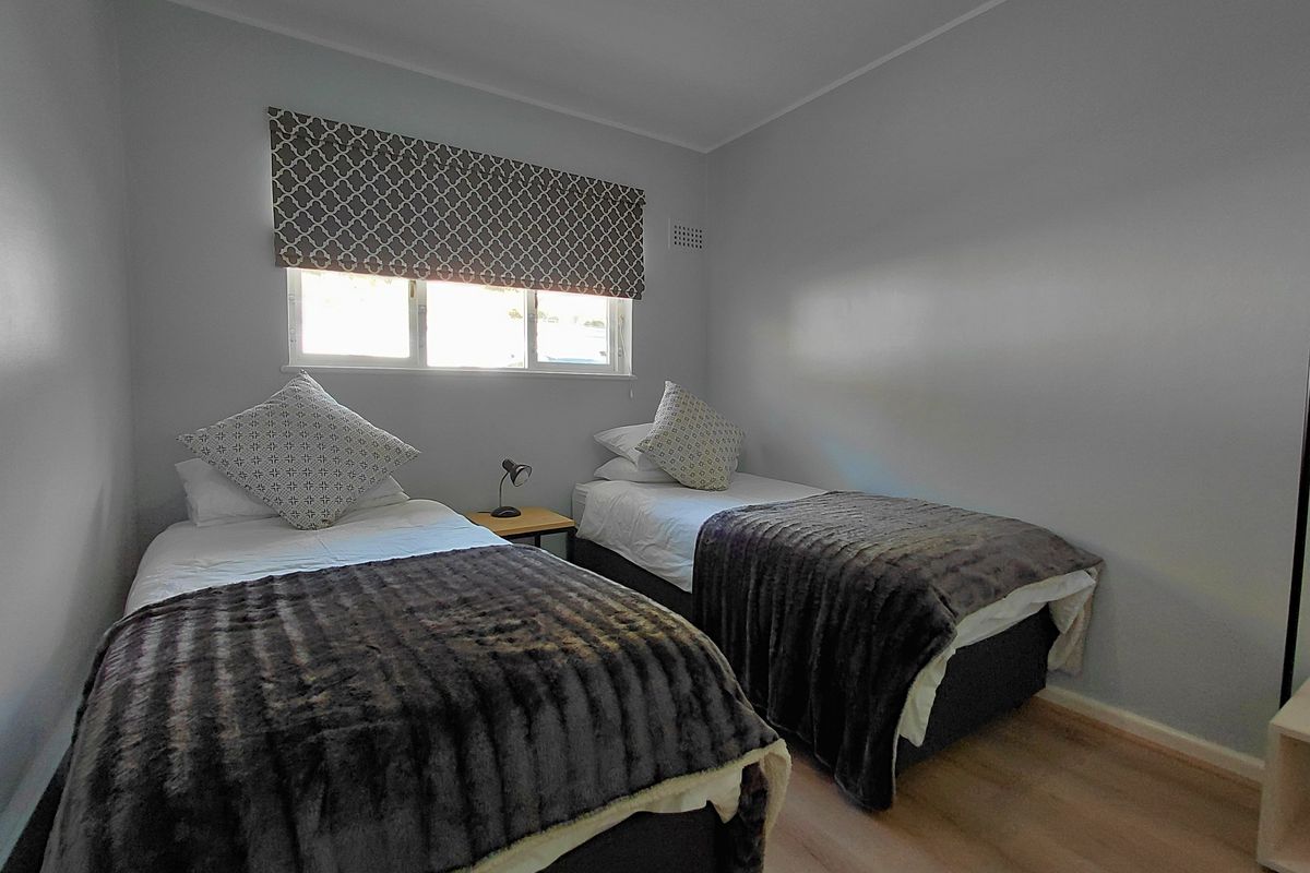 A clean and functional bedroom featuring light-toned laminate flooring, neutral wall finishes, and a window with a patterned roller blind.