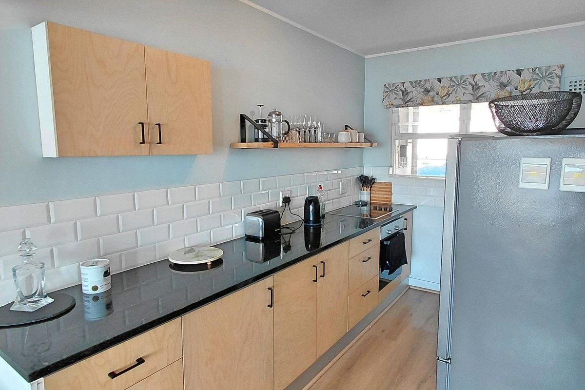 Modern galley-style kitchen featuring light plywood cabinetry, contrasting black granite countertops, subway tile backsplash, and durable laminate flooring.