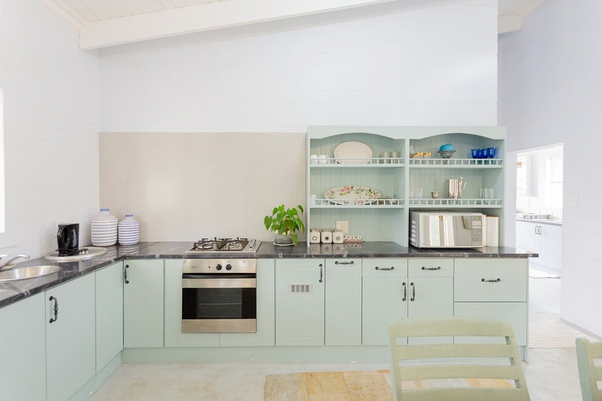 A bright kitchen featuring mint green cabinetry, dark stone countertops, a gas cooktop, built-in oven, and integrated open shelving for storage.
