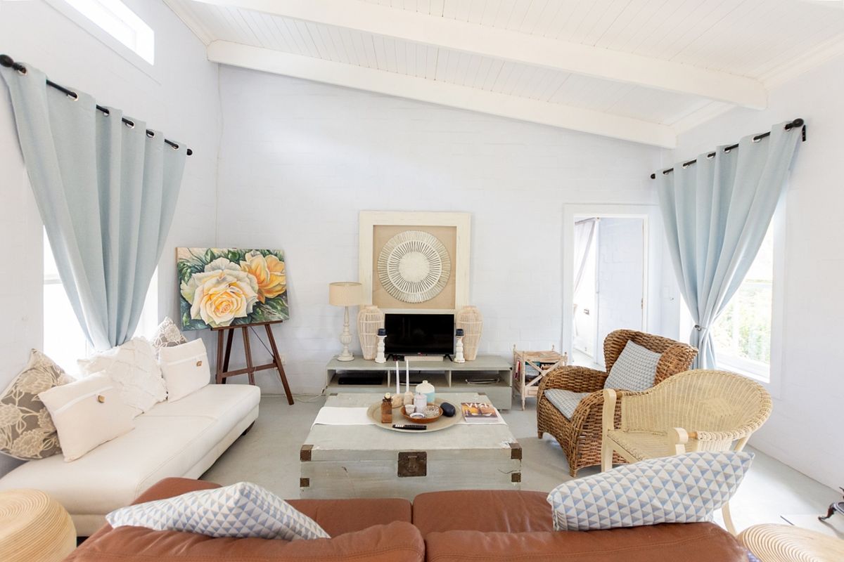 A bright and airy living room featuring a high vaulted ceiling with exposed timber beams and painted brick walls.
