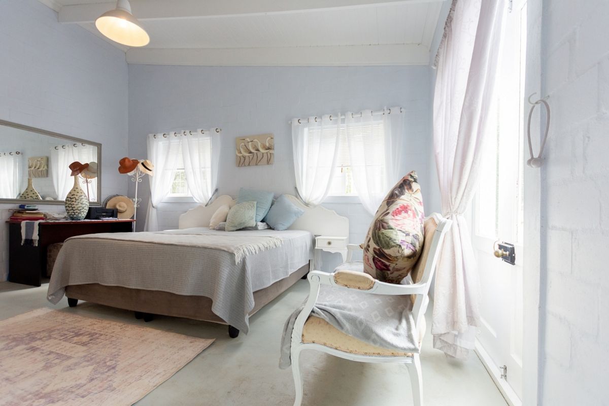 A bright bedroom featuring painted masonry walls, exposed beam ceilings, and natural light through multiple windows and a side door.