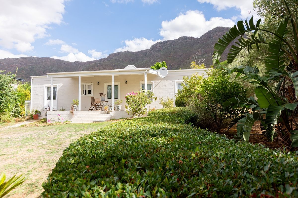 A charming single-story home featuring a covered patio, painted brick exterior, and a well-maintained garden set against a scenic mountain backdrop.