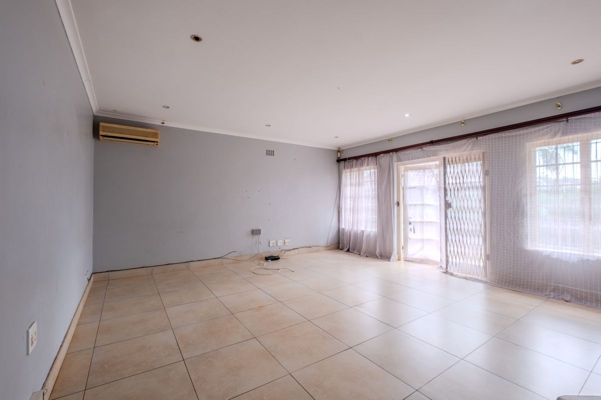 Spacious, empty living room featuring neutral tiled flooring, recessed lighting, and a wall-mounted air conditioning unit, with direct access to the exterior via sliding doors.