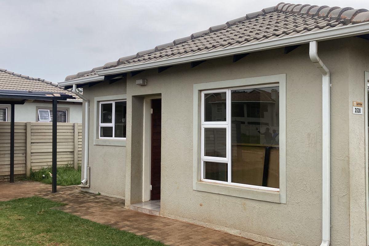 Rear view of the house featuring a paved patio area, tiled roof, and modern aluminium window frames with a sliding door entrance.