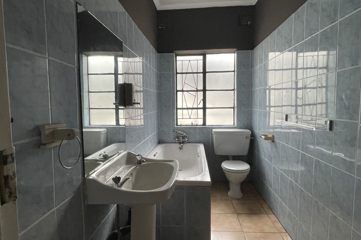 A dated bathroom featuring a pedestal basin, built-in bathtub, and full-height blue ceramic wall tiling with a neutral floor finish.