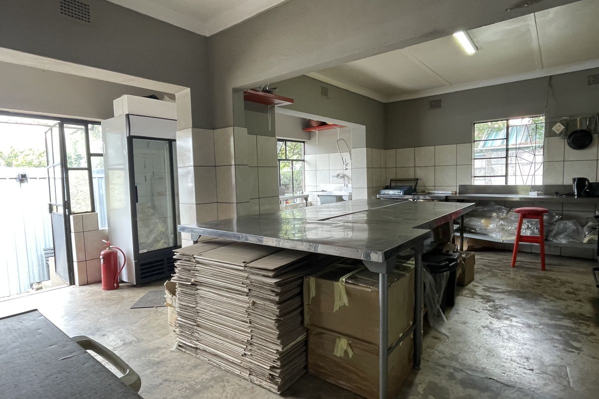 A functional commercial-style kitchen space featuring stainless steel work surfaces, tiled splashbacks, and industrial lighting, suitable for food preparation or utility use.