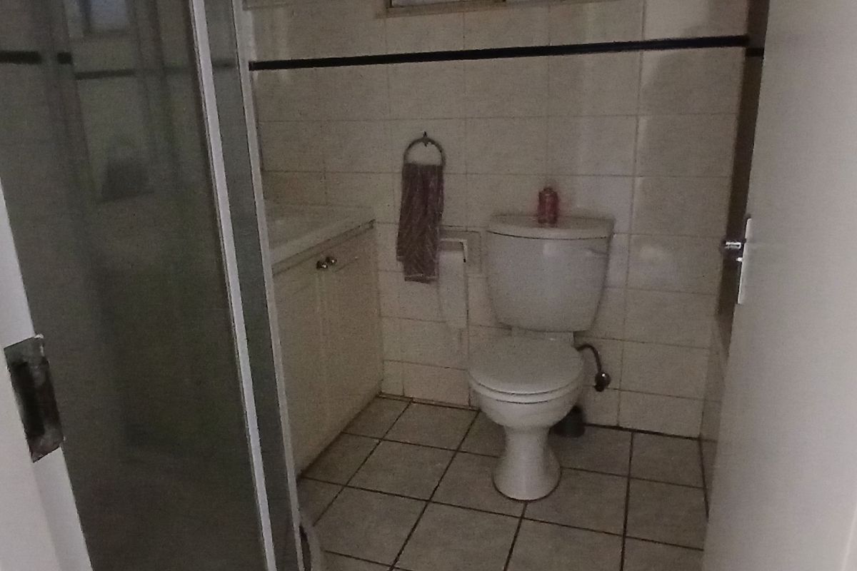 A compact bathroom featuring a shower enclosure, a vanity unit with a basin, and a standard toilet, finished with dated wall and floor tiles.