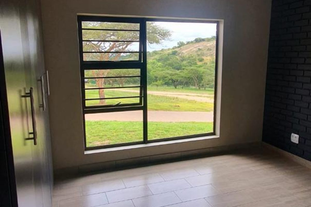 A bright, empty bedroom featuring modern tiled flooring, built-in cupboards, a striking black brick feature wall, and scenic views through the aluminium window.