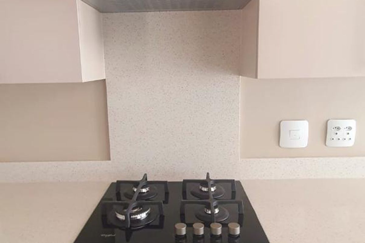 A modern kitchen featuring a built-in oven, gas hob, and extractor fan set within clean, contemporary cabinetry and stone benchtops.