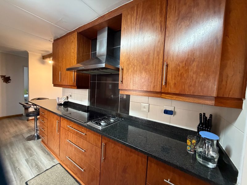 A functional kitchen featuring warm-toned wooden cabinetry, granite countertops, and a combination gas and electric hob with a stainless steel extractor fan.