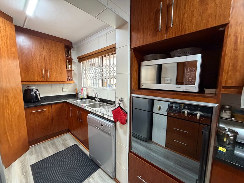 A functional kitchen featuring warm-toned wooden cabinetry, dark countertops, a built-in oven and microwave, and a window with security bars.