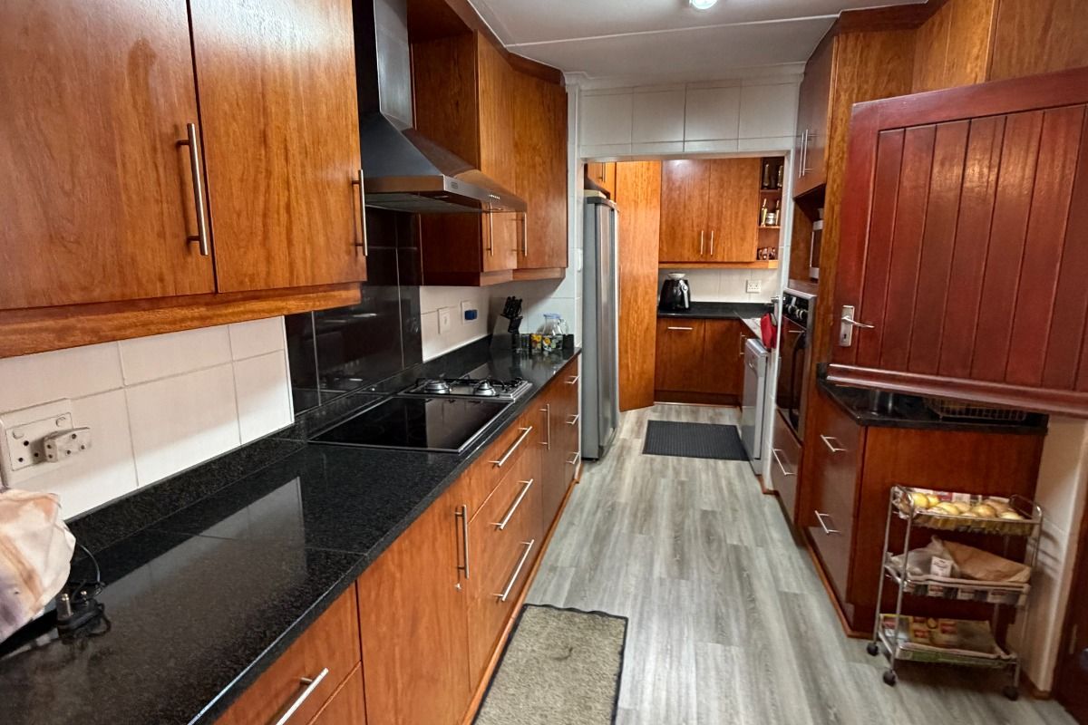 A functional kitchen featuring warm-toned wooden cabinetry, contrasting black granite countertops, modern laminate flooring, and integrated cooking appliances.